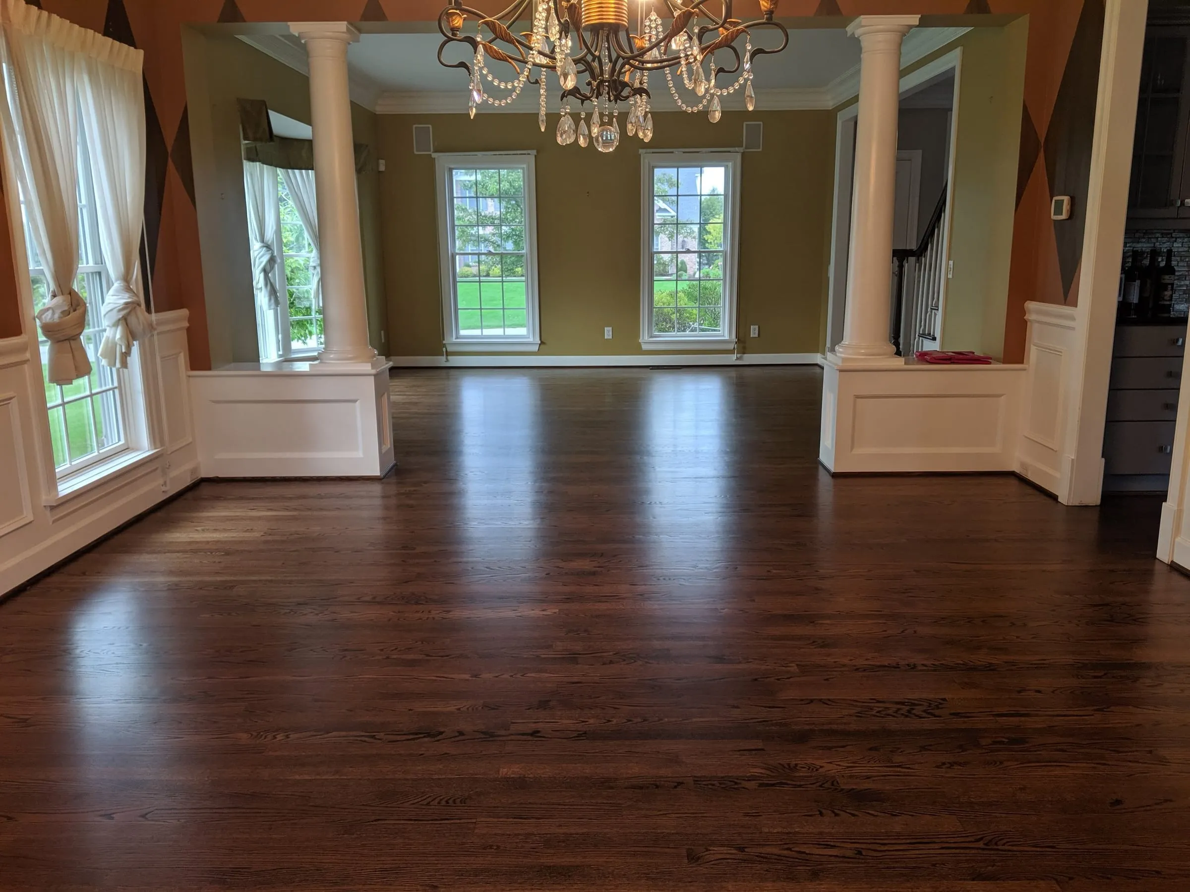 Dark-stained hardwood floor gleaming in a formal dining room with columns and a chandelier